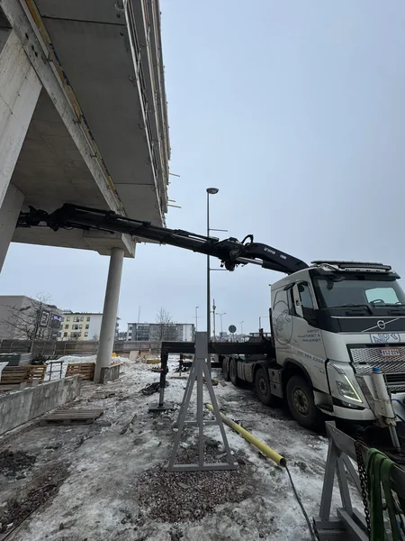 Nosturiauto ja puomi betonirakenteen alla työmaalla.