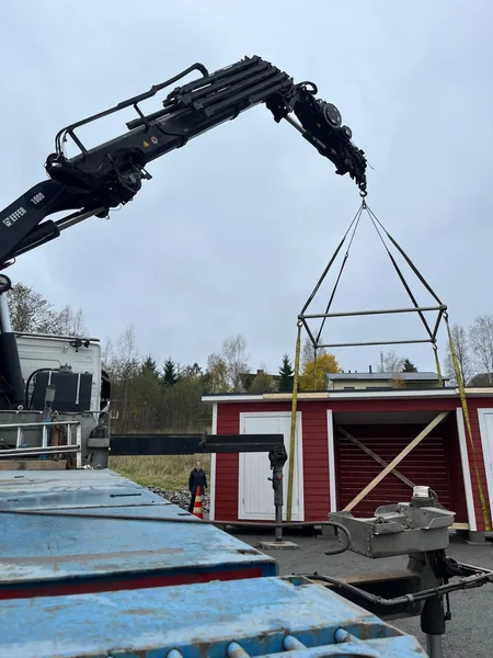 Punainen pienrakennus nosturin varassa kuljetuslavan vieressä.