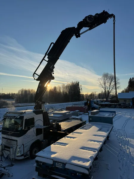 Nosturiauto lumisella työmaalla matalan auringon valossa.